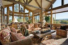 luxury great room of rustic mountain home with reclaimed log walls and timber beams towards windows and Wyoming views
