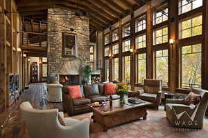 living room of luxury mountain timber frame towards fireplace and wall of windows looking out to fall colors