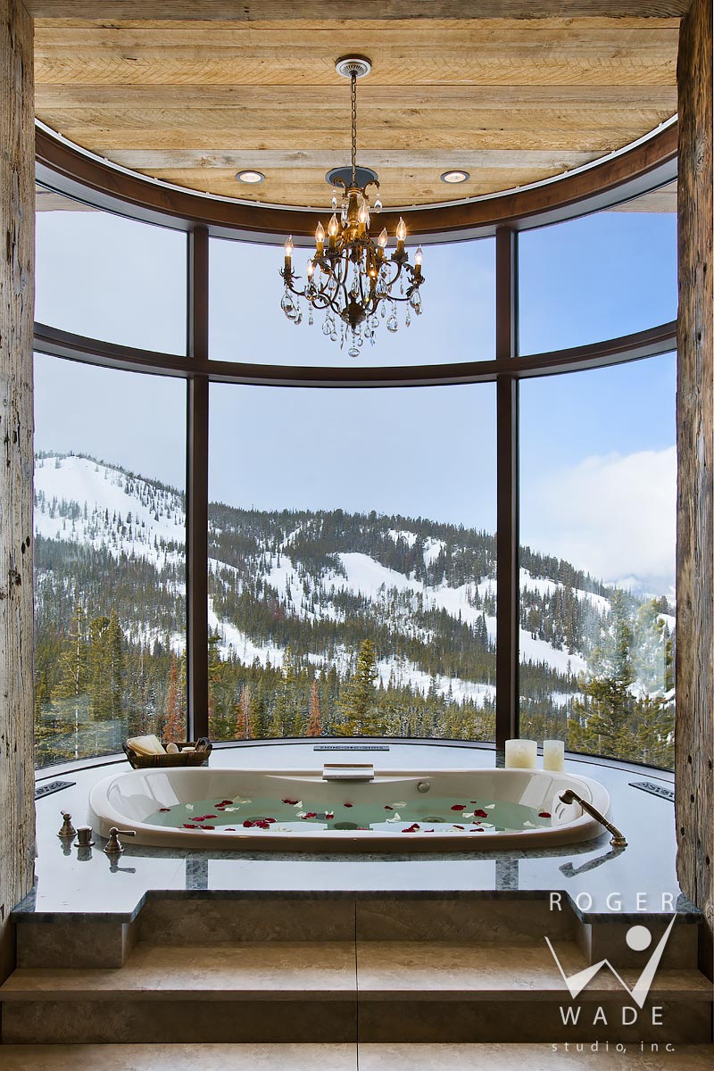 mountain modern interior design, master bathroom tub, looking out curved window to winter scenery and ski resort, big sky, montana
